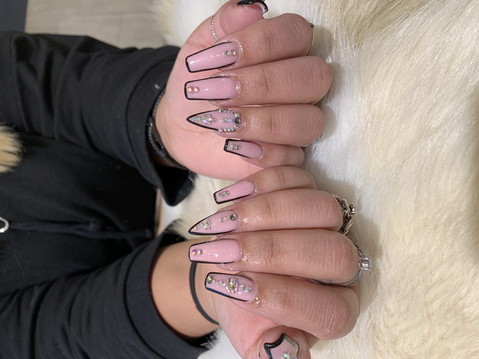 Baby pink nails with black outlines and iridescent rhinestone accents