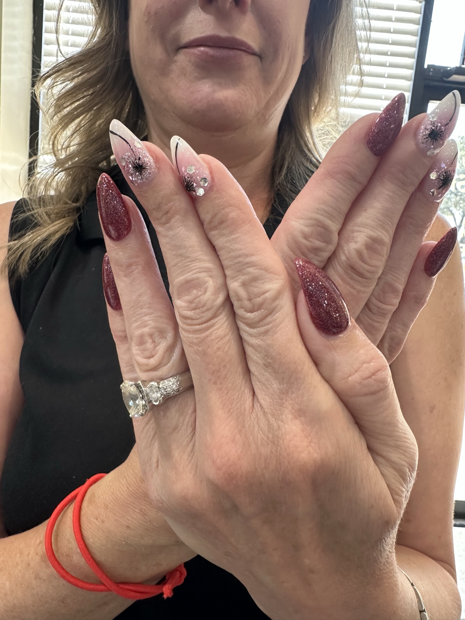 Stiletto nails with burgundy glitter and dandelion designs on pale tips