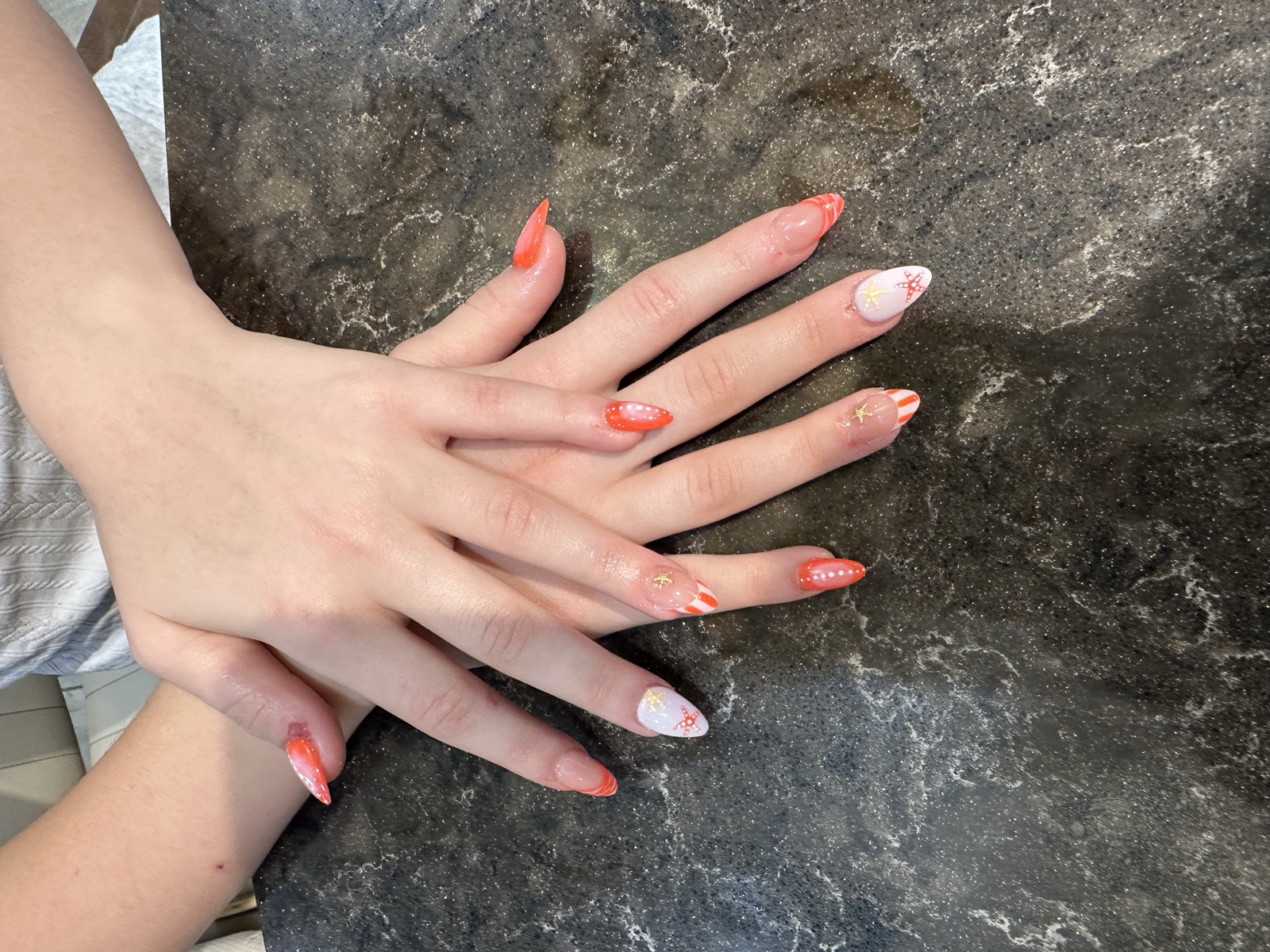 Almond nails with coral French tips, starfish, and gold star accents