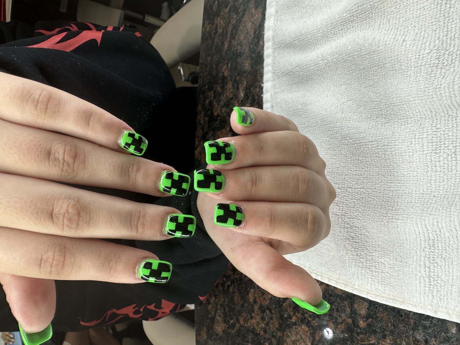 Square nails with bright green polish and black pixel-block nail art
